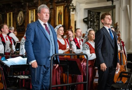 Zbliżenie na Dyrektora zespołu "Mazowsze" wraz z Solistą, w tle część orkiestry w kostiumach wilanowskich