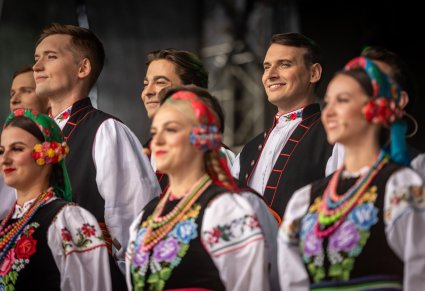 Zbliżenie na uśmiechniętych Artystów z chóru w kostiumach łowickich