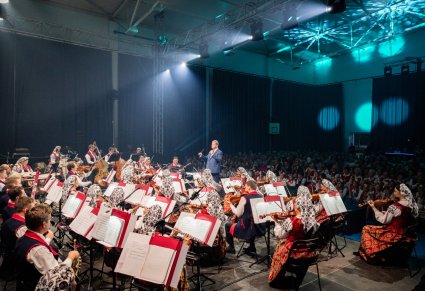 Orkiestra w kostiumach wilanowskich, Dyrygent zwrócony w jej stronę za nimi widoczna publiczność