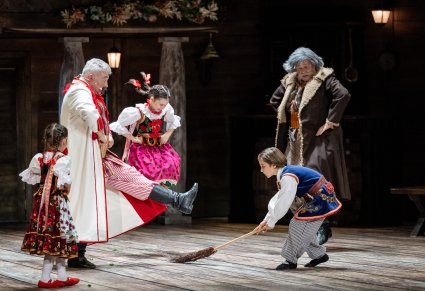 Chłopczyk w kostiumie krakowskim trzymający miotłę na scenie wraz z nim postać Ojca i Dziada i dziewczynek w kostiumach krakowskich