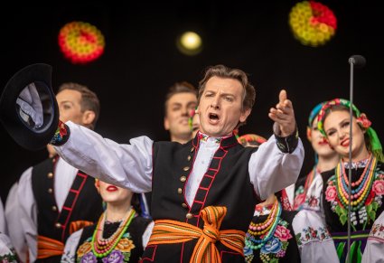 Zbliżenie na solistę, który wykonują utwór "Furman" a w tle Artyści chóru w kostiumach łowickich