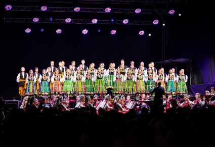 Widok na cały chór w kostiumach łowickich, z perspektywy publiczności, poniżej orkiestra w kostiumach wilanowskich i podhalańskich