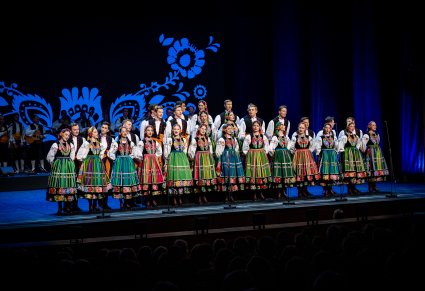 Artyści chóru w kostiumach łowickich na scenie podczas śpiewu
