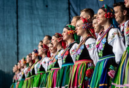 Ujęcie z profilu na rząd Artystów z chóru w trakcie śpiewu ubranych w kostiumy łowickie