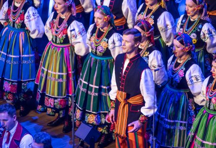 Zbliżenie na Solistę a za nim część Chóru w kostiumach łowickich ustawiona w rzędy