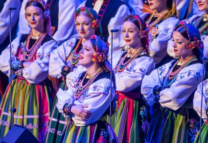 Zbliżenie na solistkę a za nią część Chóru w kostiumach łowickich