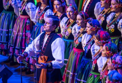 Zbliżenie na Solistę a za nim część Artystów Chóru w kostiumach łowickich