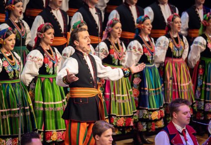 Na pierwszym planie Solista a w tle część Artystów Chóru w kostiumach łowickich podczas śpiewu