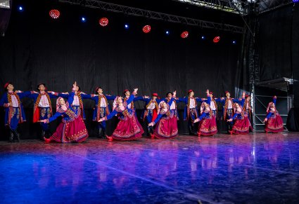 Grupa Artystów na scenie w kostiumach podegrodzkich wykonująca choreografię taneczną