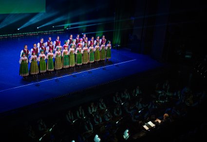 Na scenie Artyści Chóru w kostiumach kurpiowskich w trakcie śpiewu, niżej orkiestron a w nim Artyści Orkiestry wraz z maestro Jackiem Bonieckim