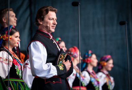 Na pierwszym planie śpiewający solista a za nim Artyści chóru w kostiumach łowickich
