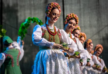 Delikatnie uśmiechnięte Artystki na scenie w kostiumach lubuskich trzymające w dłoniach winogrona