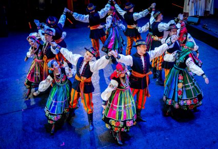 Artyści z zespołu "Mazowsze" w kostiumach łowickich w trakcie wykonywania choreografii tanecznej na scenie