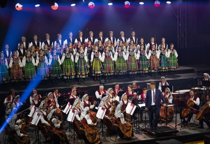 Na scenie Artyści w kostiumach łowickich, niżej Artyści Orkiestry w kostiumach wilanowskich oraz Dyrygent