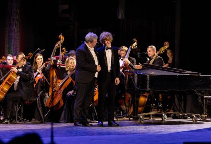 Na scenie młody pianista wraz z Dyrektorem zespołu w tle Orkiestra