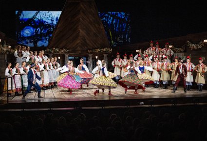 Na środku sceny Artystki w kostiumach krakowskich podczas wykonywania choreografii tanecznej, po bokach sceny artyści Chóru w kostiumach krakowskich oraz postać Kaspera i Jaśka