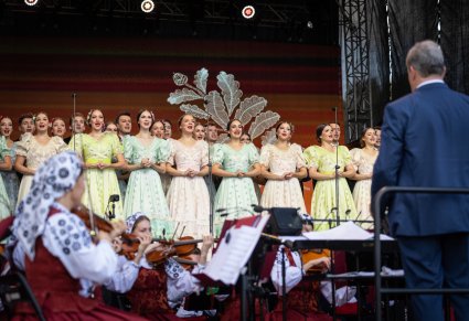 Na scenie Artyści chóru w kostiumach stylowych z końca XIX w, widoczny również Dyrygent zwrócony w stronę Orkiestry i chóru