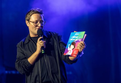 Zbliżenie na Konferansjera, który przedstawia najnowsze dzieło graficzne i tekstowe pracowników zespołu "Mazowsze", którzy stworzyli już drugą książkę dla dzieci