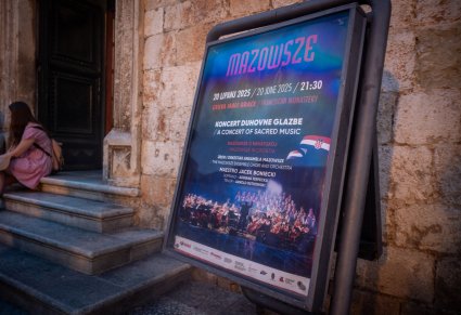 Plakat wydarzenia przed kamiennym budynkiem po lewej stronie schody a na nich kobieta w letniej sukience