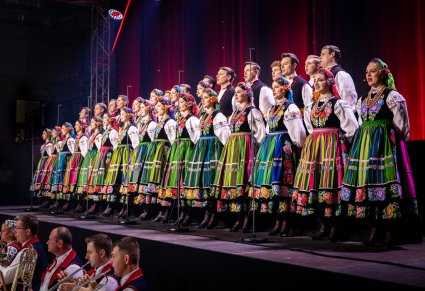 Chór w kostiumach łowickich w trakcie śpiewu. Widoczna część orkiestry dętej