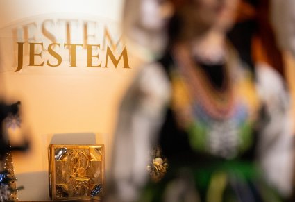 Widok na postać w kostiumie łowickim a w tle ołtarz kościoła w Zamościu z napisem JESTEM