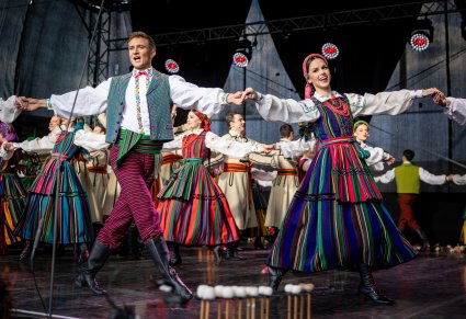 Artyści w kostiumach opoczyńskich trzymający się za ręce na scenie wykonując choreografię taneczną