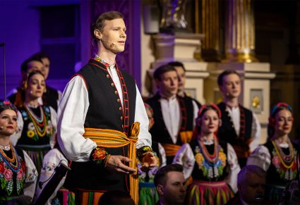 Zbliżenie na solistę chóru podczas koncertu z widocznych chórem w tle