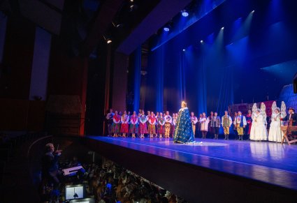 Widoczny orkiestron z Dyrygentem i częścią Orkiestry, Na scenie większa część Artystów widowiska