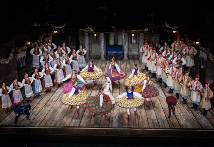 Na scenie Artystki w kostiumach krakowskich w trakcie wykonywania choreografii tanecznej, po bokach sceny Artyści Chóru w kostiumach krakowskich w trakcie śpiewu, widoczna również postać Jaśka i Kaspera