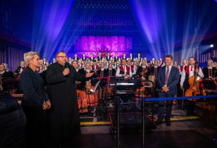 Proboszcz Parafii wypowiadający się do mikrofonu, na zdjęciu widoczny Dyrygent, Chór i Orkiestra zespołu "Mazowsze"