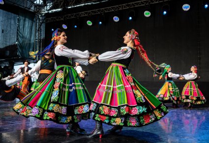 Na pierwszym planie dwie Artystki w kostiumach łowickich, które trzymają się za ręce