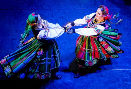 Zbliżenie na dwie Artystki z zespołu "Mazowsze" w kostiumach łowickich podczas wykonywania choreografii tanecznej na scenie