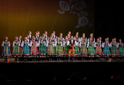 Na pierwszym planie solista wraz z zespołem w kostiumach łowickich