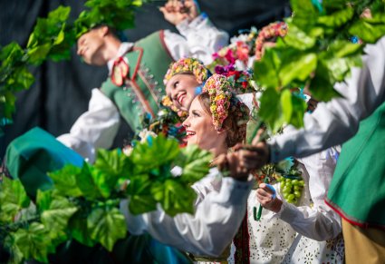 Zbliżenie na Artystów na scenie w kostiumach lubuskich trzymających w dłoniach dekoracje w kształcie winorośli