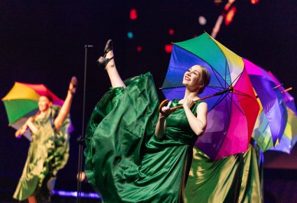Zbliżenie na Artystki w zielonych sukienkach, trzymające w ręku rozłożony kolorowy parasol, wykonujące choreografię taneczną do utworu Medley