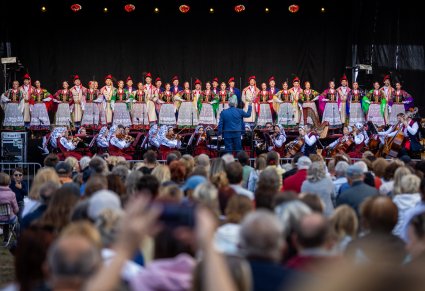 Na pierwszym planie efekt rozmazania publiczności, na drugim planie Dyrektor Jacek Boniecki, Orkiestra i chór na scenie w kostiumach krakowskich