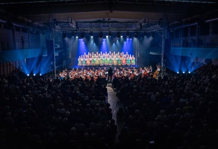 Na scenie Artyści w kostiumach łowickich, niżej orkiestra wraz z Dyrygentem, widoczna również publiczność