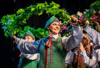 Na pierwszym planie uśmiechnięty Artysta w kostiumie lubuskim trzymający w górze winorośle