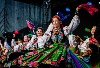 Uśmiechnięte Artystki na scenie w kostiumach łowickich wymachują chustami w stronę publiczności