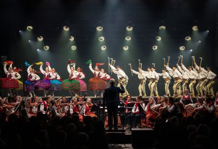 Na scenie Artyści w kostiumach podhalańskich w trakcie wykonywania choreografii tanecznej, niżej Artyści Orkiestry w kostiumach wilanowskich wraz z Dyrygentem trzymającym w górze batutę