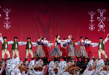 Grupa Artystów w kostiumach spiskich wykonująca choreografię taneczną, widoczna również część orkiestry w kostiumach wilanowskich