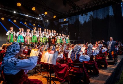 Chór w kostiumach łowickich, widoczna orkiestra na scenie