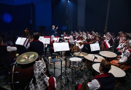 Na pierwszym planie Artyści orkiestry w kostiumach wilanowskich, w drugim planie Dyrygent zwrócony w ich stronę, trzymający w ręku batutę