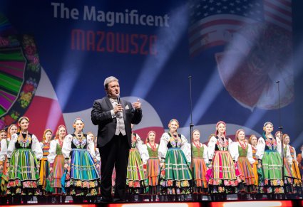 Na scenie na pierwszym planie Dyrektor zespołu, w tle Artyści w kostiumach ludowych