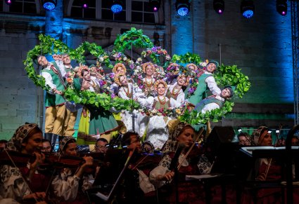 Na pierwszym planie Artyści w kostiumach lubuskich w figurze tanecznej trzymający dekorację związaną z winoroślą