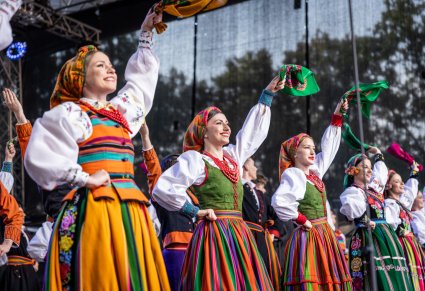 Na scenie Artystki w kostiumach ludowych machające w górze kolorowymi chustami