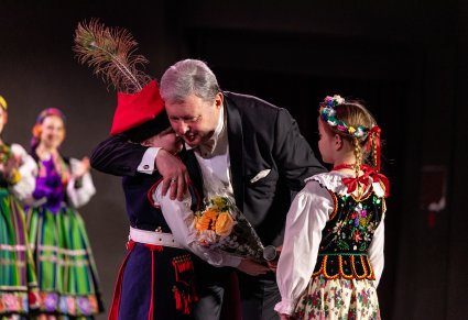Dyrektor zespołu odbierający kwiaty od dzieci w kostiumach krakowskich