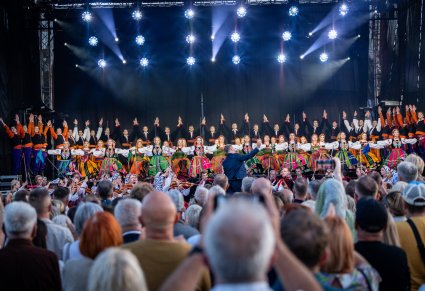Widok na balet w kostiumach łowickich i sannickich, a także na orkiestrę i dyrygenta, z perspektywy publiczności