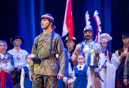 Na pierwszym planie postać Powstańca w tle reszta postaci grająca w widowisku