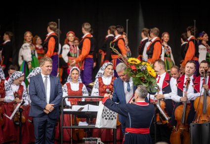 Na pierwszym planie wręczenie Dyrektorowi kwiatów, w tle orkiestra i Artyści na scenie